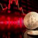 Bitcoin token standing in front of a blurred red price chart.